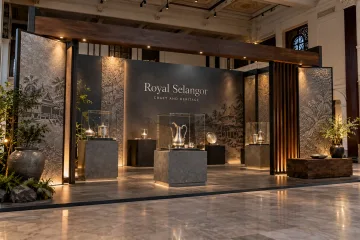 Royal Selangor heritage craftsmanship exhibition with museum-style pewter display plinths, glass cases, heritage texture panels and a sculptural entrance frame