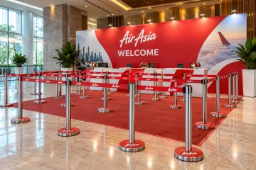 AirAsia branded q pole registration lanes with realistic waist-height brushed-metal retractable-belt queue poles with round weighted bases and red belts repeatedly printed AirAsia in white, arranged in a clear serpentine registration lane, coordinated branded base wraps and a printed registration backdrop